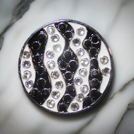 Golf ball marker with black, white, and silver pattern on a marble surface